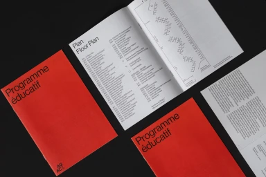 Open brochure and two red paper booklets with black typography titled Programme educatif arranged on a dark surface.
