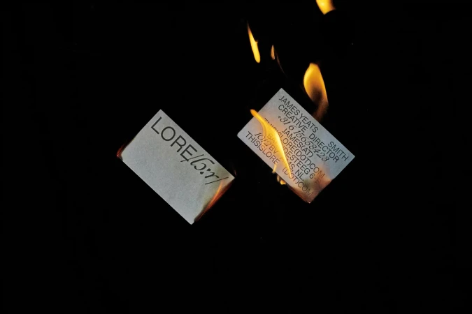 Close-up of burning business cards against a black backdrop, emphasizing texture and destruction in a minimalist composition.