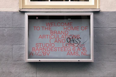 Signage for Studio Lore with red typography inside a silver frame mounted on a gray concrete block wall