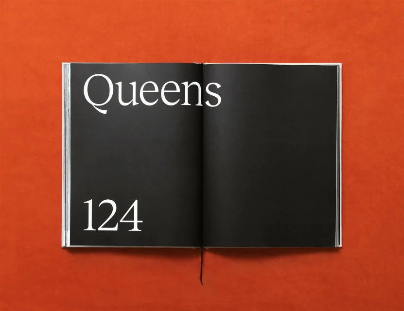 Open book with black pages on a red surface displaying the words 'Queens 124' in a clean, modern, white sans-serif typeface.