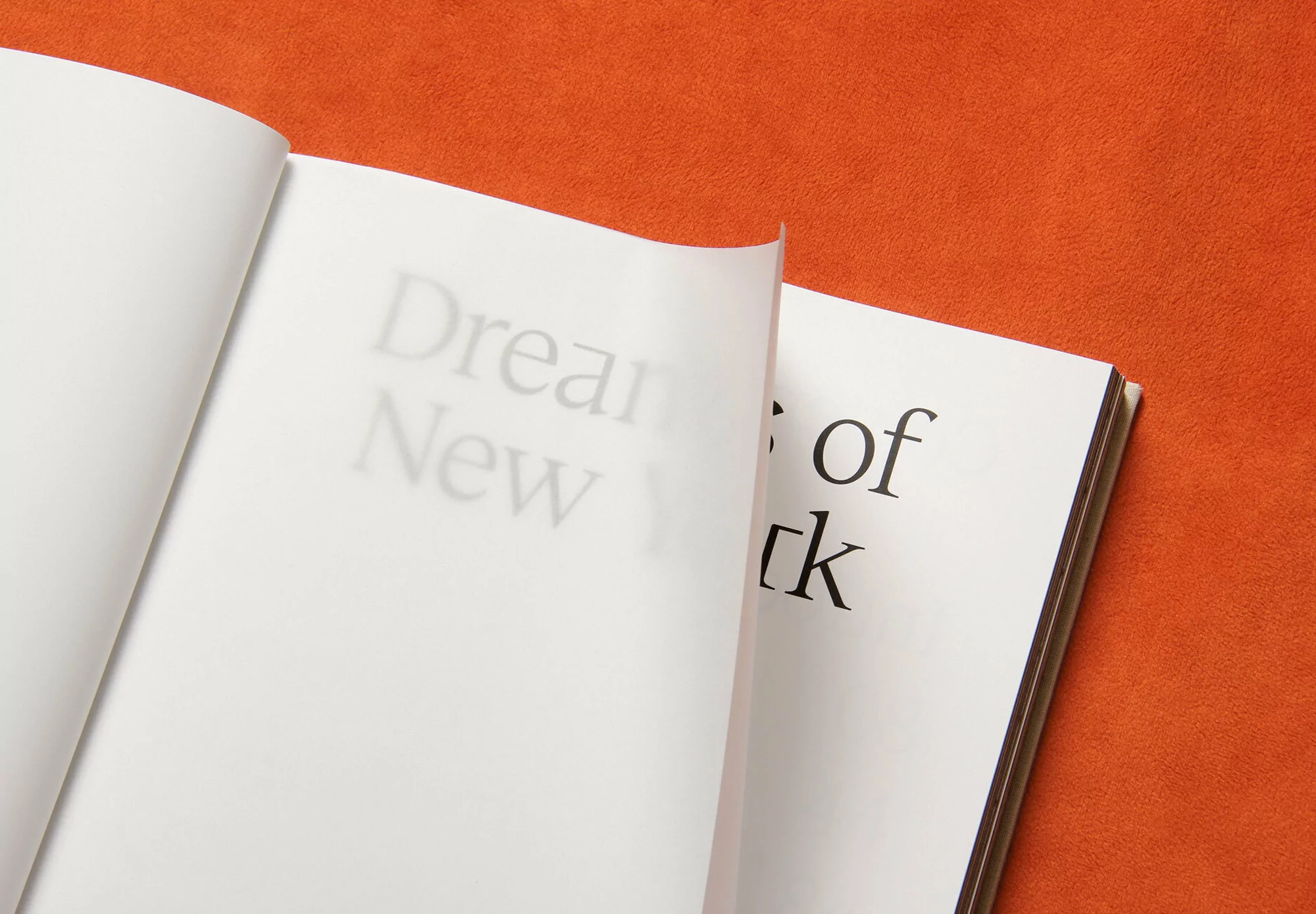 Open book with the text 'Dreams of New York' on its pages, resting on an orange textured surface. Focus is on typography.