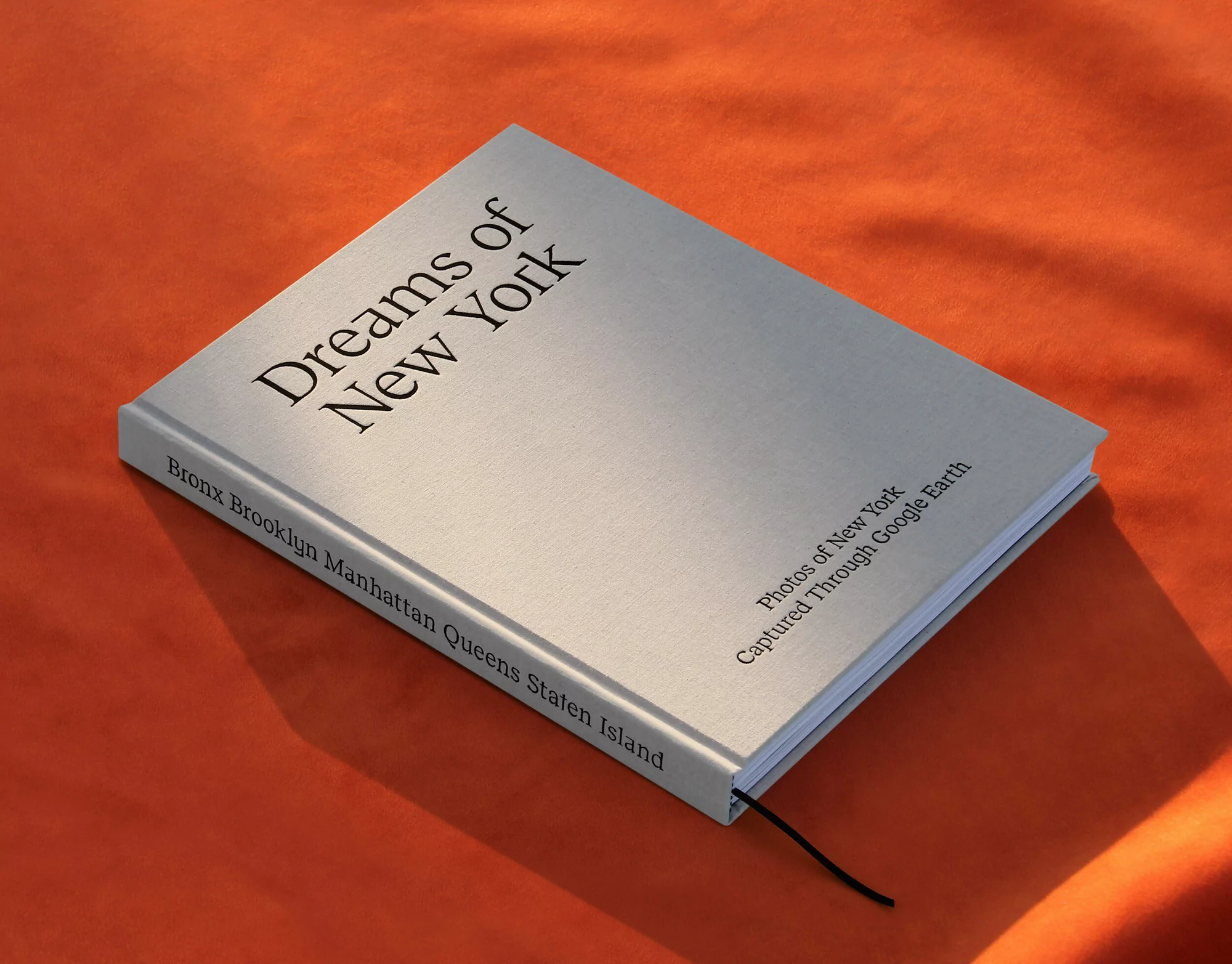Elevated view of a book titled 'Dreams of New York' with visible text listing boroughs, captured with natural lighting on orange fabric.