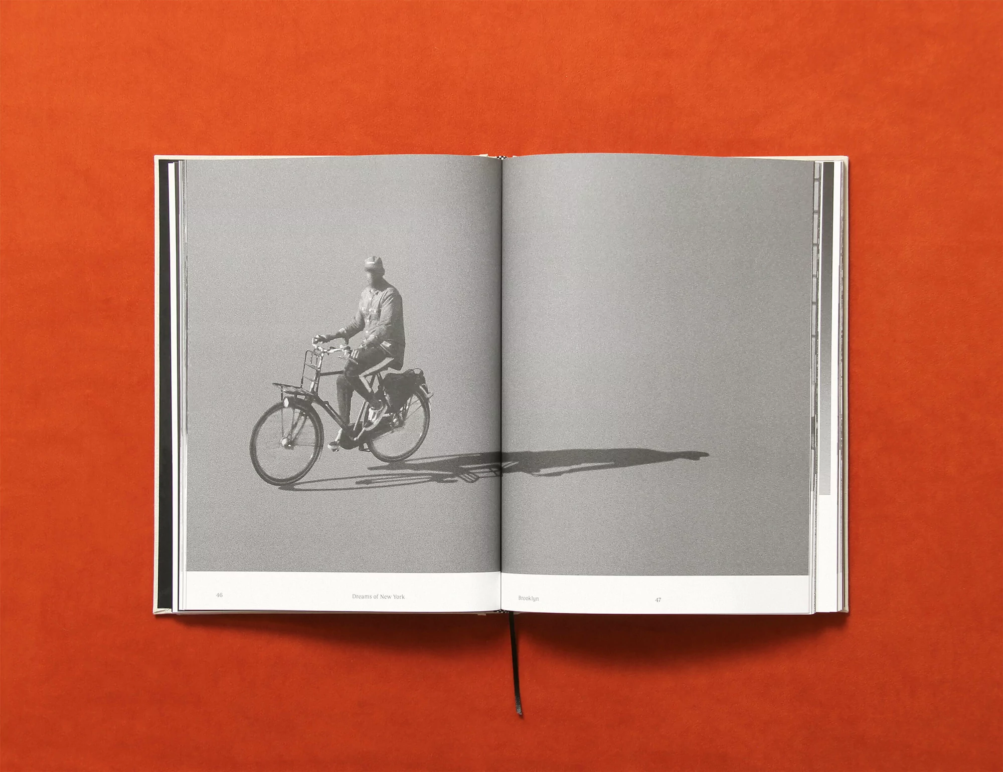Monochrome image of an open book featuring a photo of a person riding a bicycle, set against a gray backdrop, and an orange background.