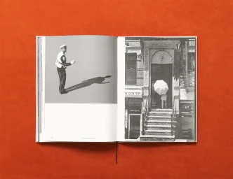 An open photography book on a textured orange surface displaying black and white imagery on both pages.