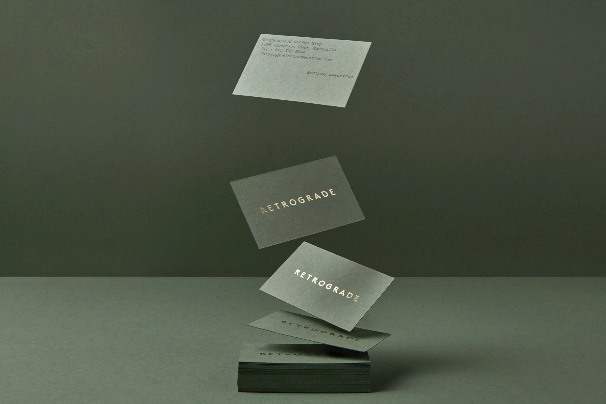 Elevated view of a stack of business cards with the word Retrograde in gold lettering, floating above a minimalist green surface.