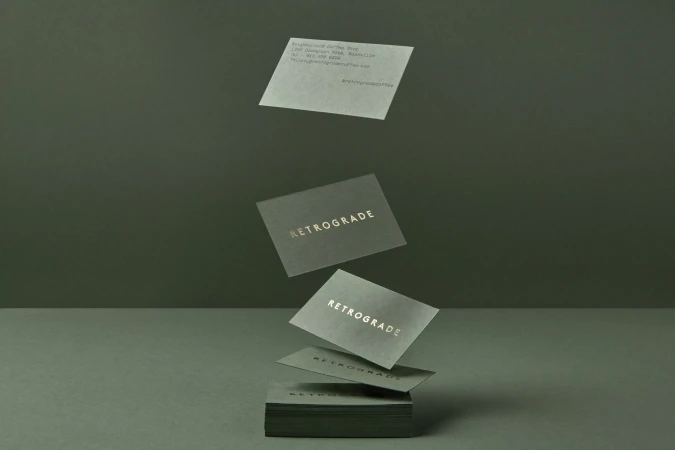 Elevated view of a stack of business cards with the word Retrograde in gold lettering, floating above a minimalist green surface.