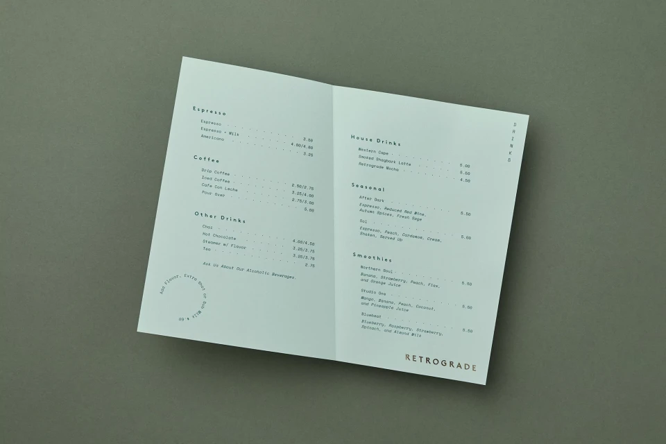 Open, white cafe menu featuring espresso, coffee, house drinks, seasonal drinks, and smoothies sits on a flat, neutral surface.