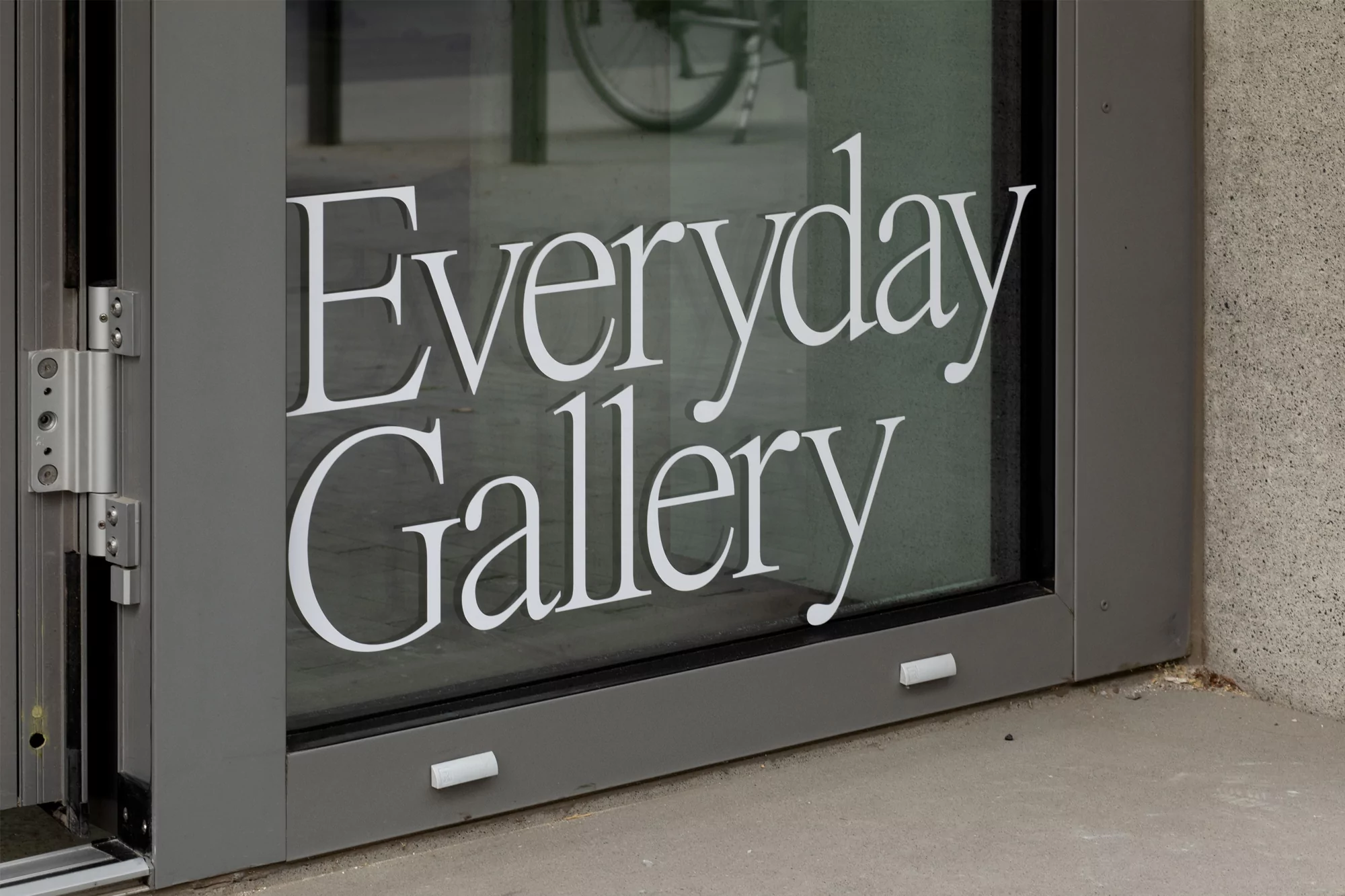 Exterior view of a gray building entrance with glass doors displaying the white, sans-serif text 'Everyday Gallery'.
