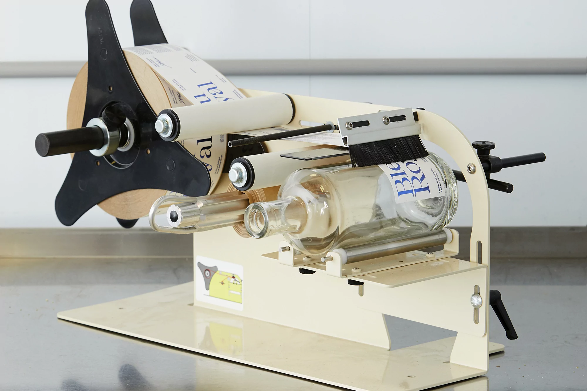 A bottle labeling machine applies labels to glass bottles, showcasing industrial automation in a sterile, brightly lit environment. 