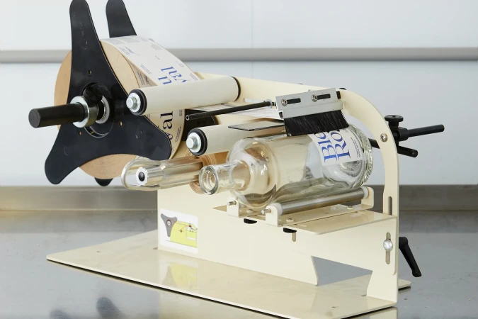 A bottle labeling machine applies labels to glass bottles, showcasing industrial automation in a sterile, brightly lit environment. 