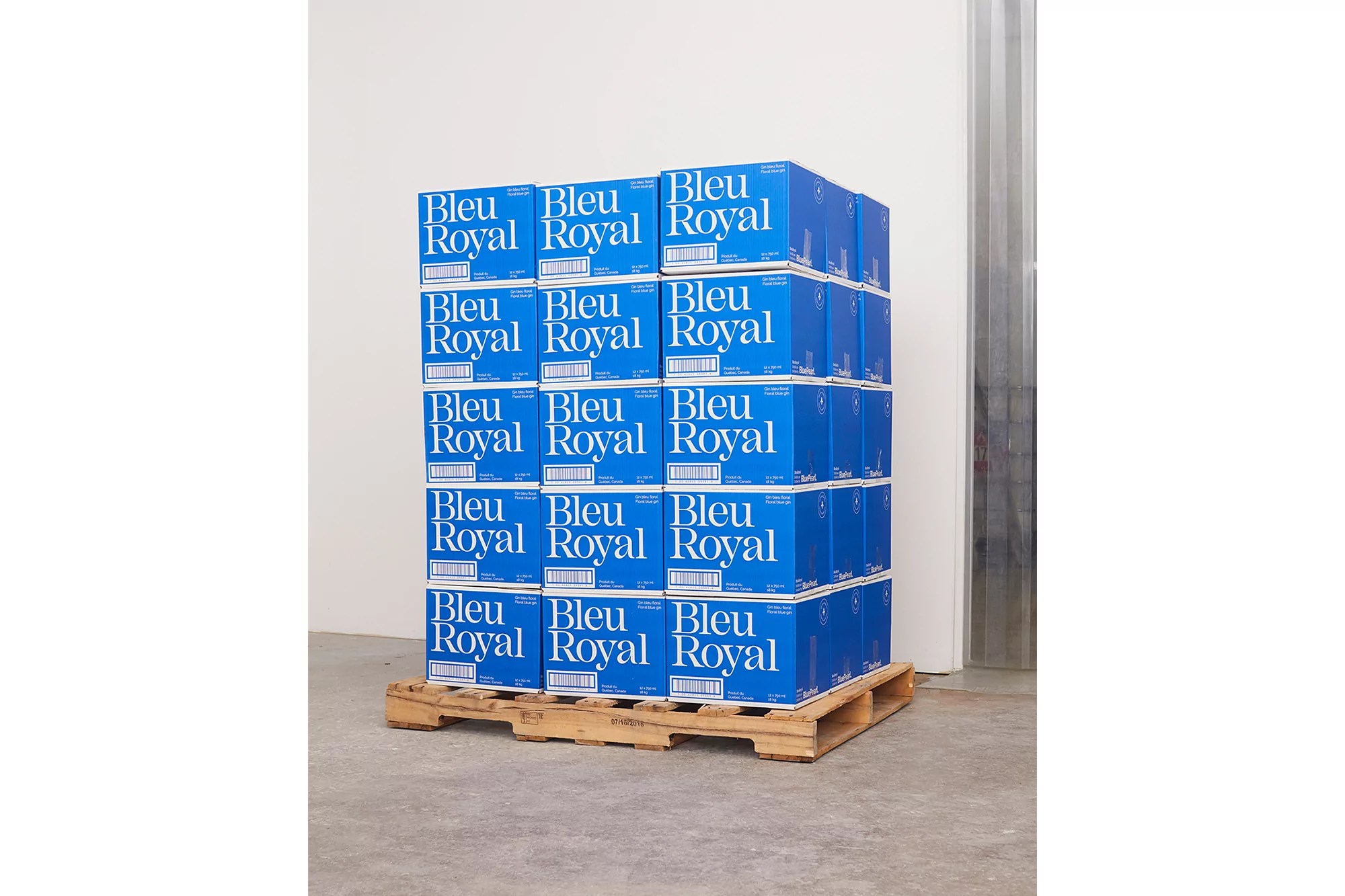 Stack of blue boxes with white text on a wooden pallet against a white wall with a metal column in an indoor setting.