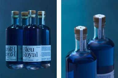 Blue glass bottles of BleuRoyal gin with wooden cork stoppers and white labels on a dark blue background