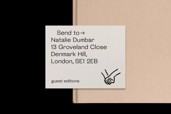 Close-up of an off-white address card featuring black text and hand graphic on a peach book cover against a black background.