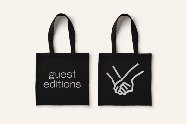 Two black canvas tote bags displayed on a light cream background, featuring white text and a graphic illustration.