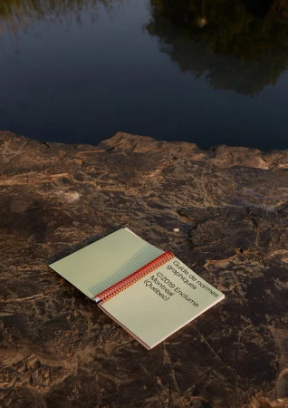 Open guidebook on rocky surface near water's edge, featuring text about graphical standards from 2019, in Montreal, Quebec.