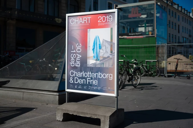 Street-level advertisement poster for the CHART 2019 art event featuring building and draped blue cloth in Copenhagen, Denmark.