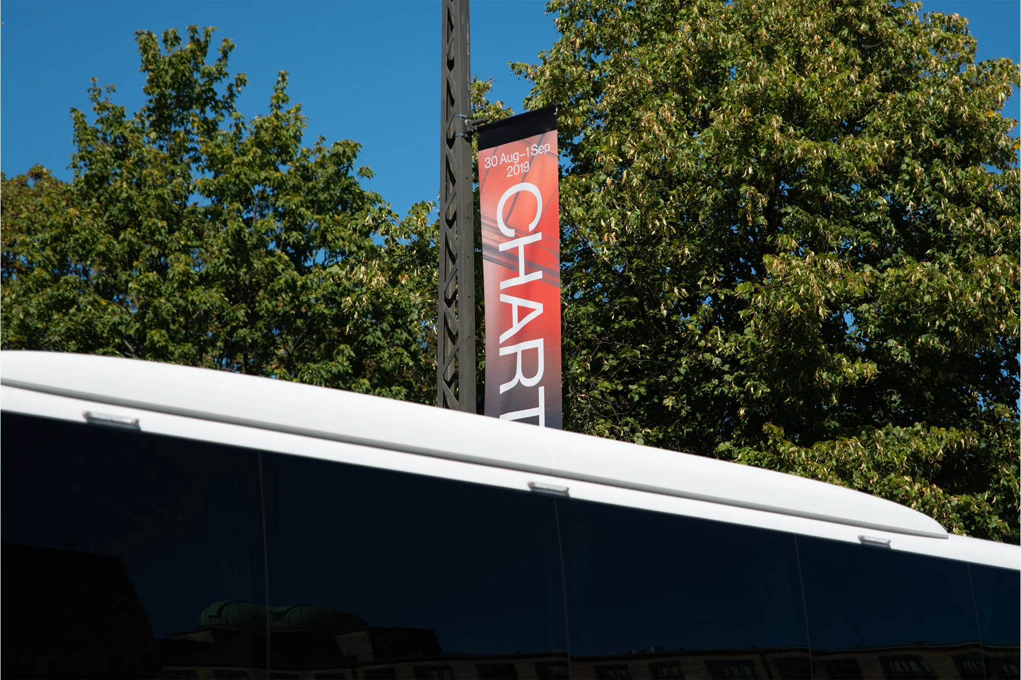 Banner for 'Chart' art event against a background of green trees and blue sky is partially obscured by white bus roof.