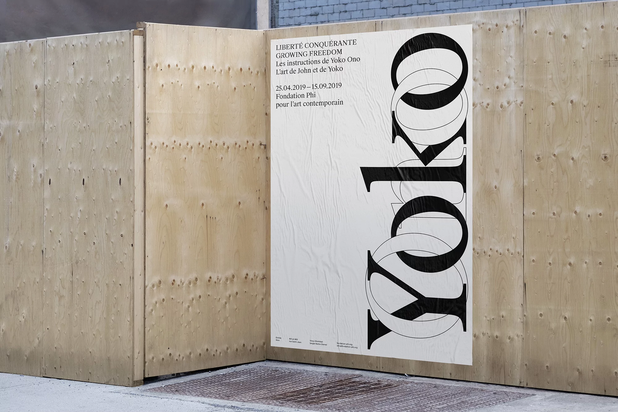 Art exhibit promotion poster of Yoko Ono art on a wooden wall. The poster has large black text and exhibition dates.