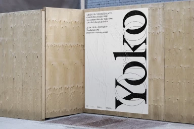 Black and white Yoko Ono exhibition poster pasted on a wooden construction hoarding exterior.