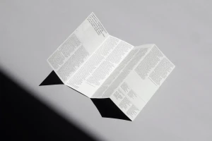 A folded printed brochure with typography resting on a plain grey surface casting a sharp dark shadow