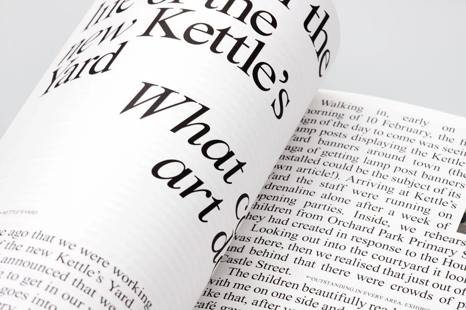 Open magazine spread with bold black typography on white pages, featuring article excerpts and design elements, creating a modern aesthetic.