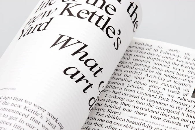 Open magazine spread with bold black typography on white pages, featuring article excerpts and design elements, creating a modern aesthetic.