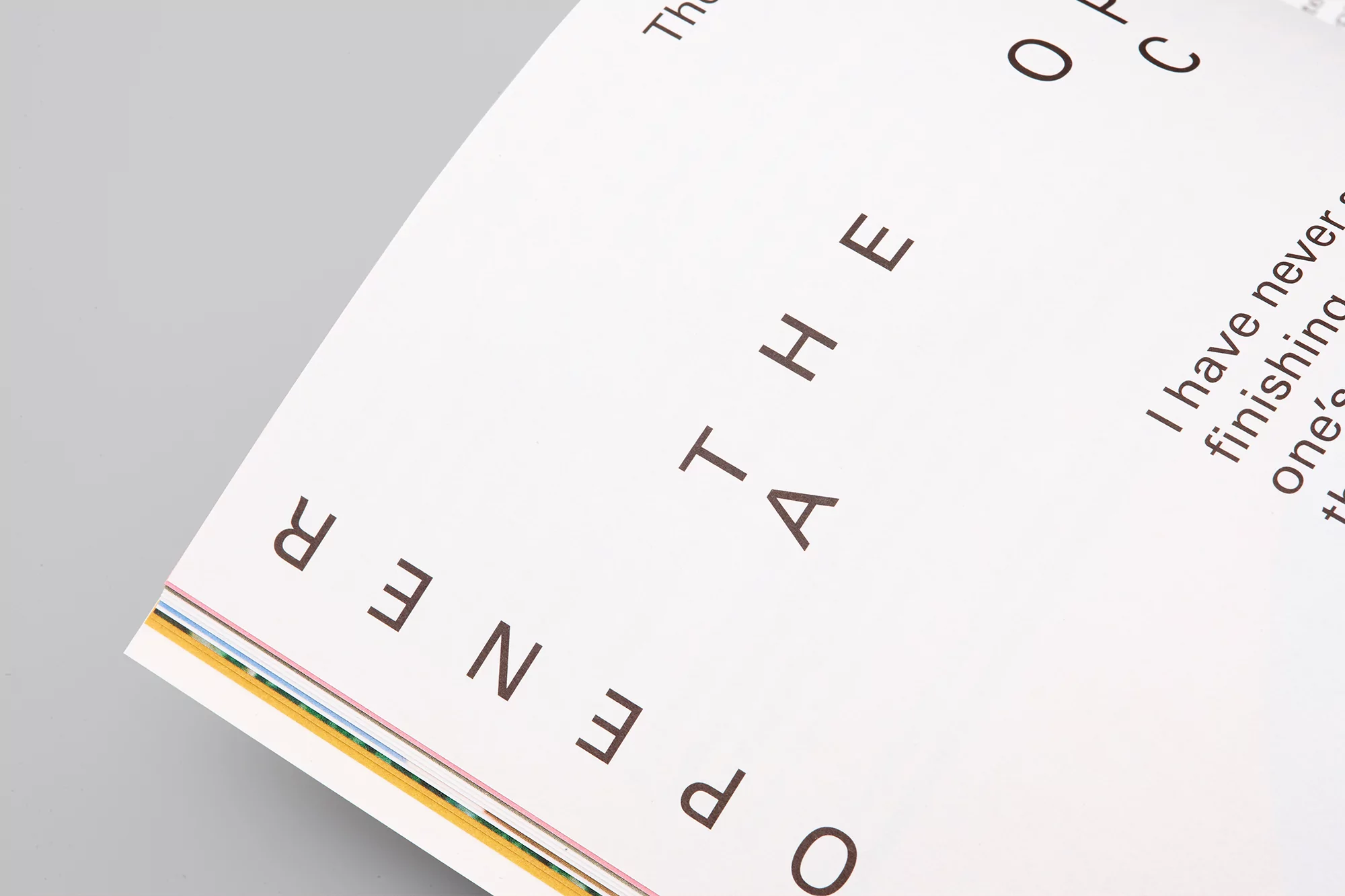 Open magazine page with text, “The Opener,” brown font, white pages, and a multi-colored edge. Angled shot, simple background.