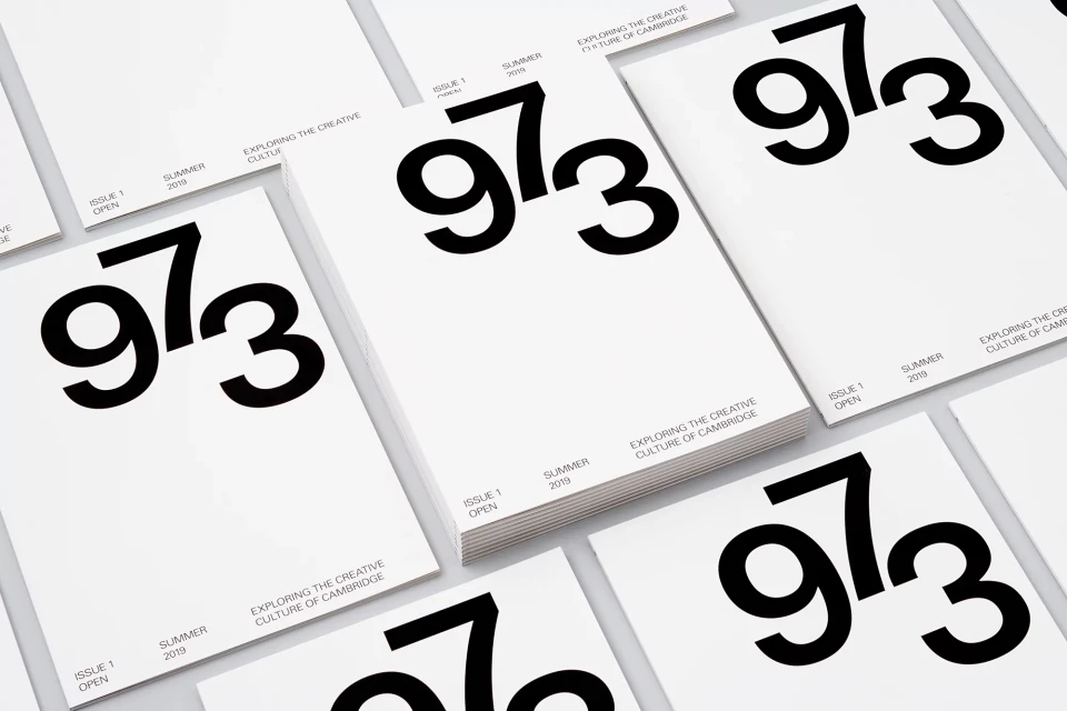 Stack of '973' magazines on white background in an overhead shot. Bold black and white design for creative culture publication.