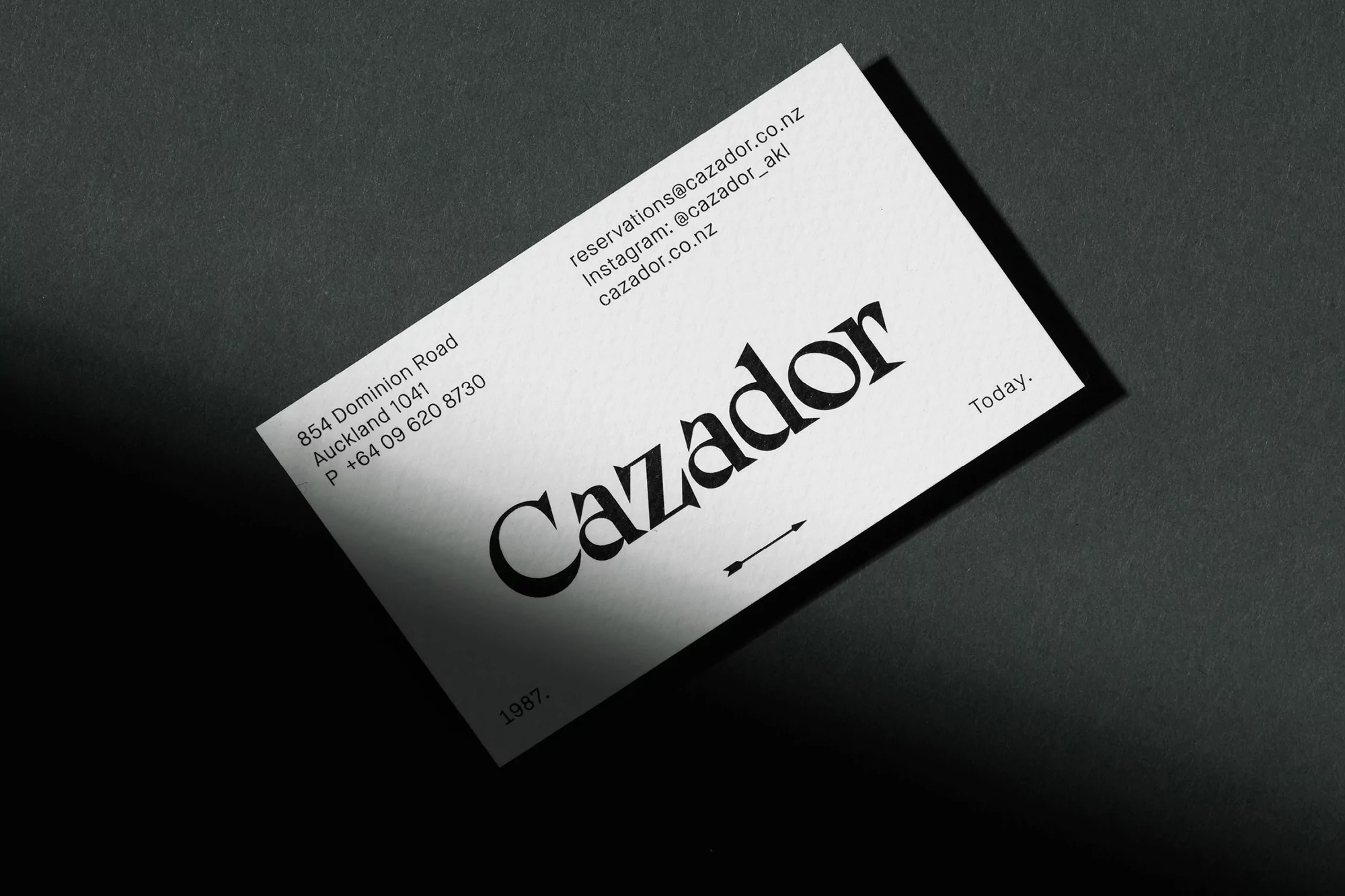 Close-up of a modern, minimalist business card for 'Cazador' on a textured gray surface, featuring clean typography and elegant design.