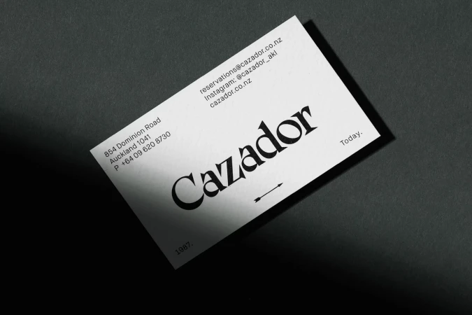 Close-up of a modern, minimalist business card for 'Cazador' on a textured gray surface, featuring clean typography and elegant design.