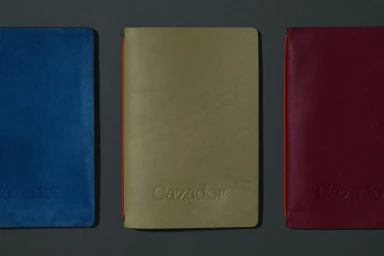 Three leather notebooks in blue olive green and burgundy arranged on a dark grey surface for Cazador brand identity project
