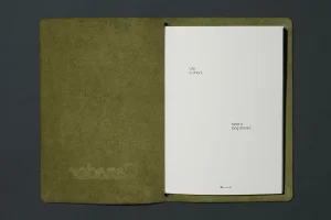 An open olive green leather notebook revealing white pages with minimalist typography against a dark background.