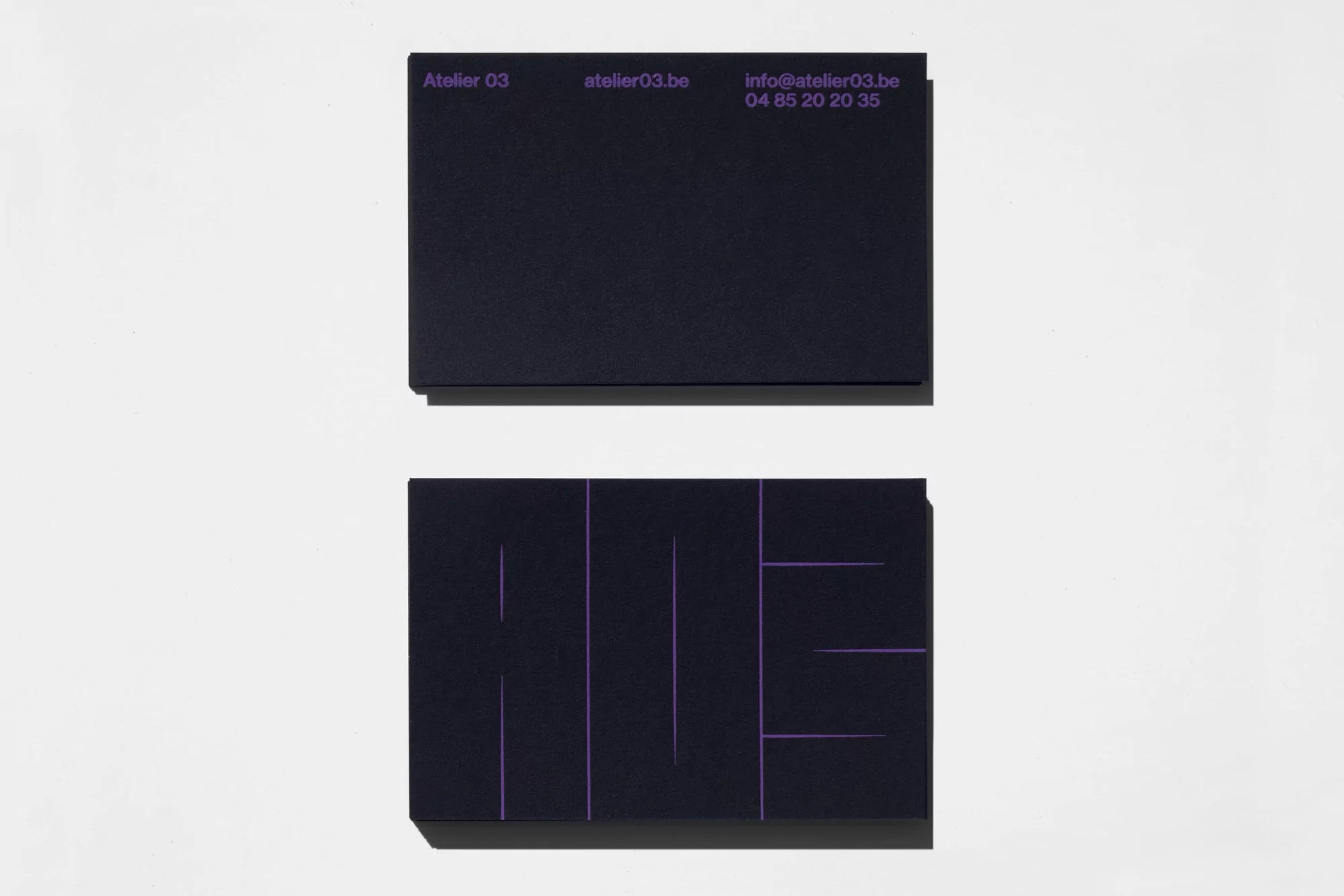 Stack of business cards. The top card shows Atelier 03 branding, contact email, and phone number, while the bottom card displays a logo.