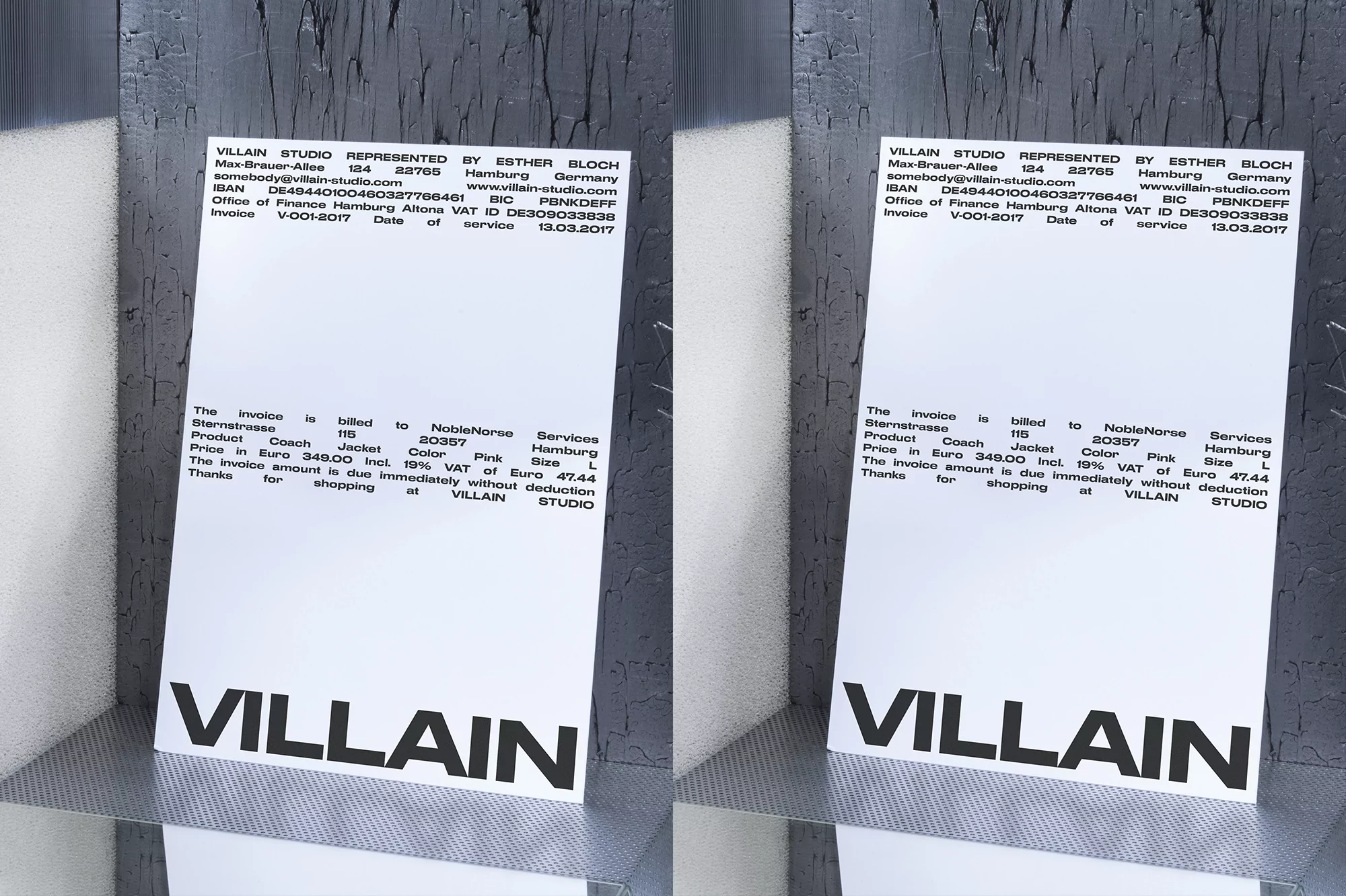 Two identical business cards on a reflective surface against a textured wall, featuring the word 'VILLAIN' and contact details.