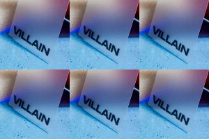 Frosted acrylic branding card displaying the word VILLAIN in bold black lettering against a textured blue and grey concrete surface.