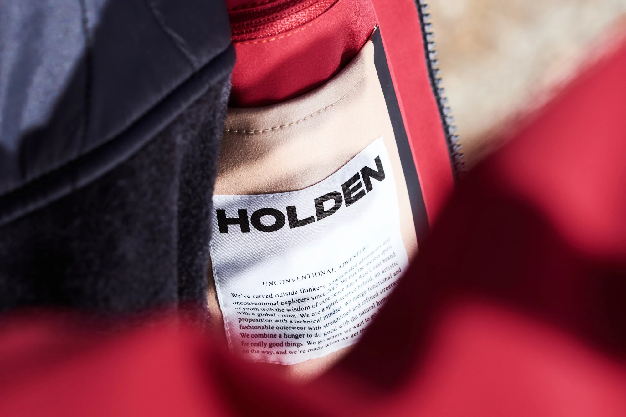 Close-up of a Holden brand label stitched into the inside of a red jacket, showcasing the brand's logo and philosophy statement.