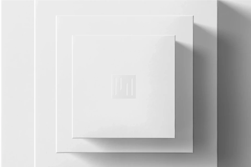 Overhead shot of nested square white boxes, minimalist design with geometric logo, casting soft shadows in a modern setting.