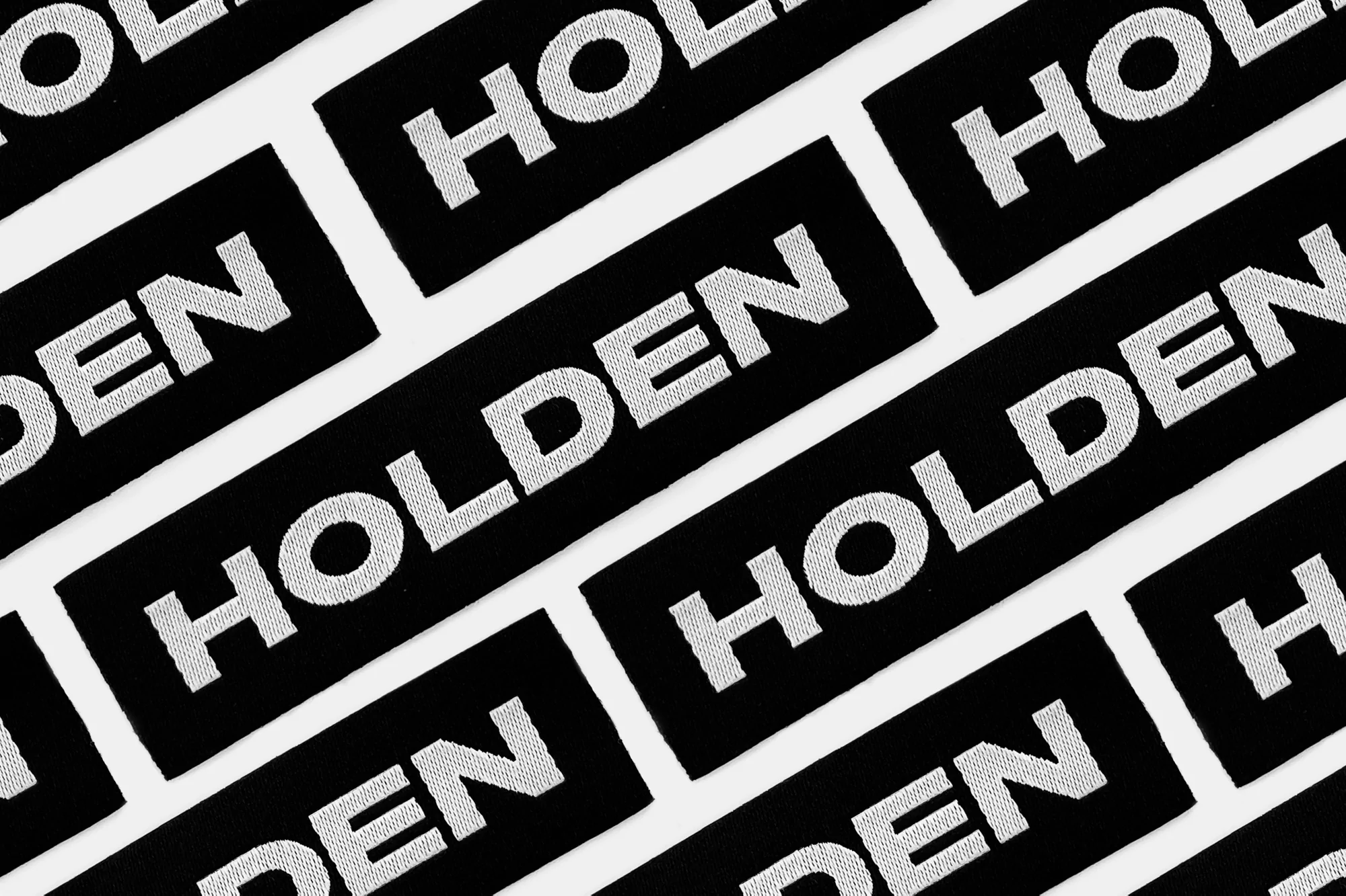 Multiple black rectangles angled on a white background with the word 'HOLDEN' repeated in white text, creating a repeating pattern.