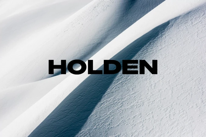 A stark aerial view captures the brand 'Holden' in bold black letters against a backdrop of snow-covered mountain dunes, emphasizing texture.