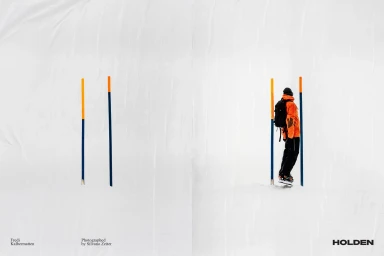 Snowboarder in an orange jacket standing between blue and yellow poles on a snowy white background with Holden logo.