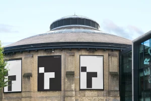 Round brick building exterior featuring large graphic posters mounted on the walls under a glass domed roof