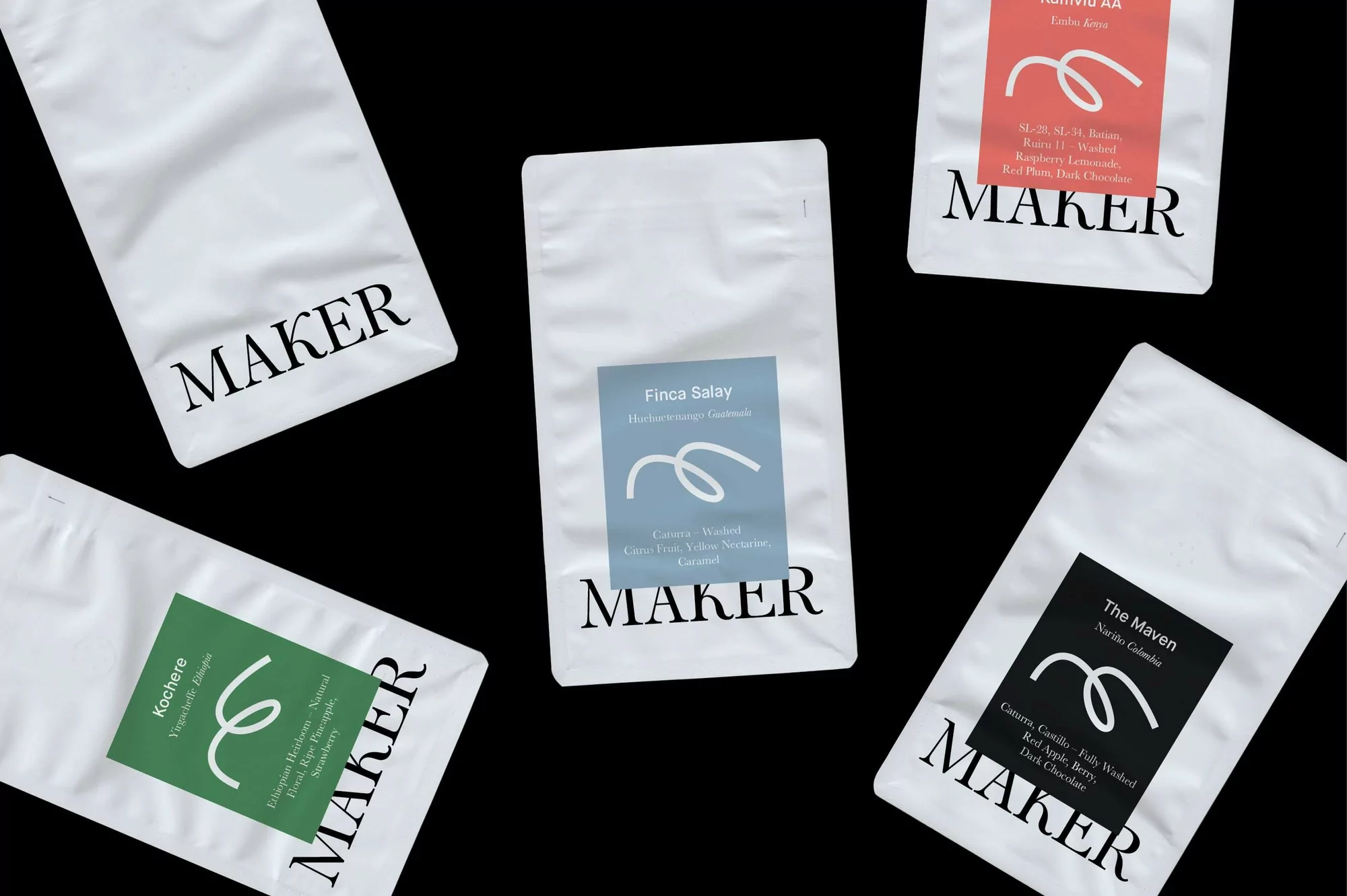 Multiple white sealed bags of Maker brand coffee beans with flavor and origin details arranged on a stark black background.