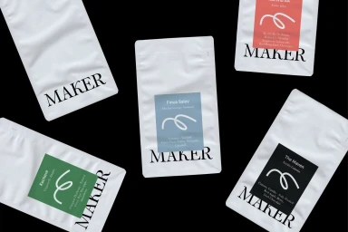 Five white coffee bags with Maker branding arranged on a solid black background, featuring colored flavor labels.