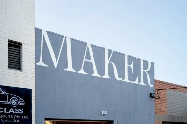 Exterior shot of a grey building facade featuring large white typography reading MAKER under a clear sky