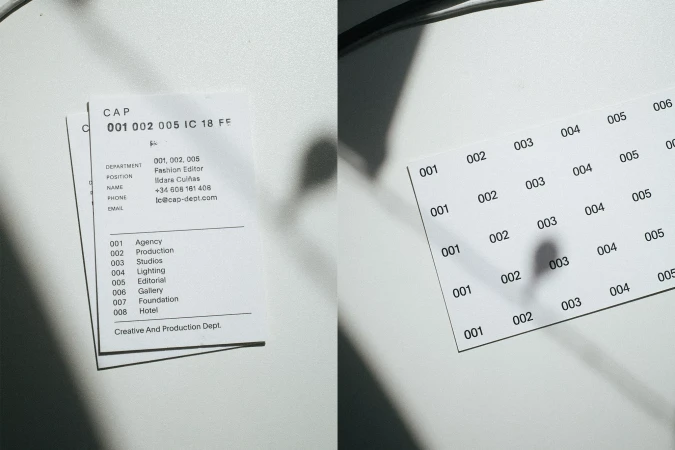 Close-up of two business cards on a white surface with shadow and text related to fashion, agency, studios, production, lighting, gallery.