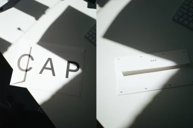 White branded CAP envelope on a desk under harsh sunlight casting diagonal shadows