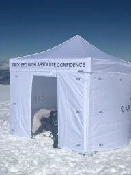 White branded canopy tent set up on a snowy mountain terrain under a clear sky.