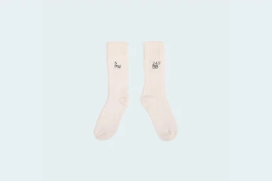 A pair of cream white ribbed crew socks featuring black typography laid flat against a pale background