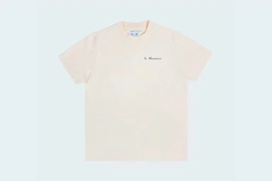 Plain light cream short-sleeve t-shirt laid flat against a solid pale background with small dark chest text branding