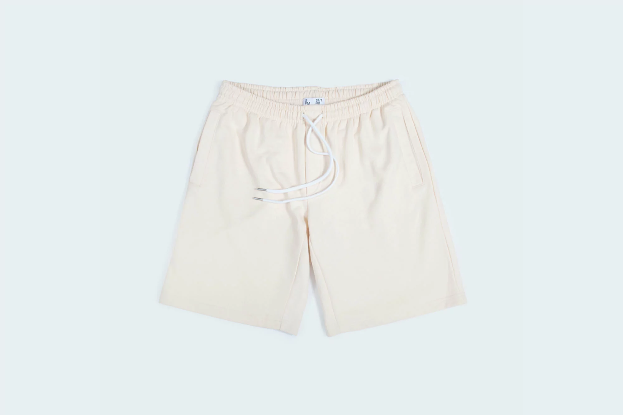 Studio shot of light beige shorts with drawstring, elastic waistband, and pockets, isolated on a light blue background.
